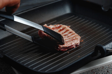 A large piece of fresh beef meat cooked in a grill pan. Stripes on the meat. Fluted frying pan.