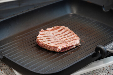 A large piece of fresh beef meat cooked in a grill pan. Stripes on the meat. Fluted frying pan.