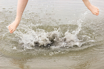 Feet jumping in the water on the lake shore.