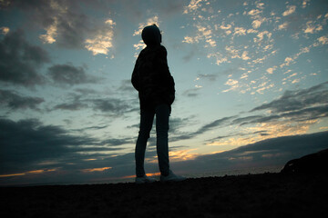 A silhouette of a woman on the ocean shore at sunset