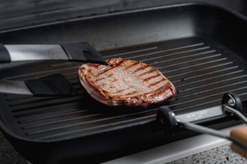 A large piece of fresh beef meat cooked in a grill pan. Stripes on the meat. Fluted frying pan.