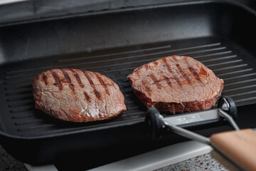 A large piece of fresh beef meat cooked in a grill pan. Stripes on the meat. Fluted frying pan.