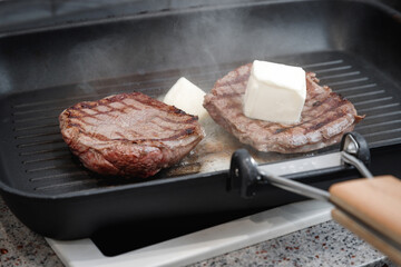 A large piece of fresh beef meat cooked in a grill pan. Meat is fried in butter. Stripes on the meat. Fluted frying pan.