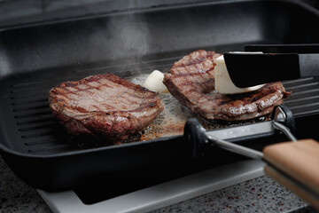 A large piece of fresh beef meat cooked in a grill pan. Meat is fried in butter. Stripes on the meat. Fluted frying pan.