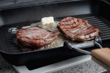 A large piece of fresh beef meat cooked in a grill pan. Meat is fried in butter. Stripes on the meat. Fluted frying pan.