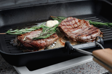 Fresh beef meat cooked on a grill pan. Meat is fried in butter. Steak with rosemary. Stripes on the meat. Fluted frying pan.