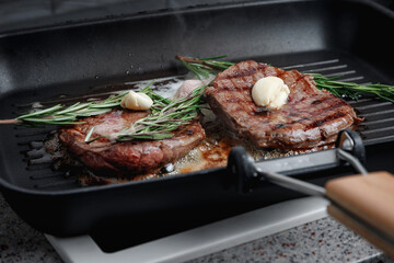 Fresh beef meat cooked on a grill pan. Meat is fried in butter. Steak with rosemary. Stripes on the meat. Fluted frying pan.
