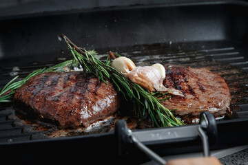 Fresh beef meat cooked on a grill pan. Meat is fried in butter. Steak with rosemary. Stripes on the meat. Fluted frying pan.