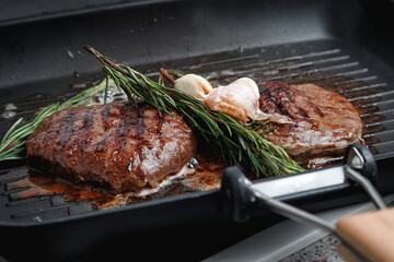 Fresh beef meat cooked on a grill pan. Meat is fried in butter. Steak with rosemary. Stripes on the meat. Fluted frying pan.