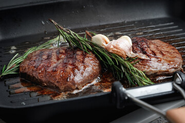 Fresh beef meat cooked on a grill pan. Meat is fried in butter. Steak with rosemary. Stripes on the meat. Fluted frying pan.