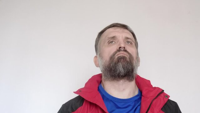 Man with white wall behind him puts on red coat and zips it.