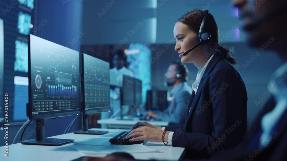 Poster Happy Confident Technical Customer Support Specialist Having a Headset Call while Working on a Computer in a Dark Monitoring and Control Room Filled with Colleagues and Display Screens.