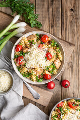 Chicken pasta salad with roasted and sun-dried tomatoes, topped with green onion slices and grated cheese