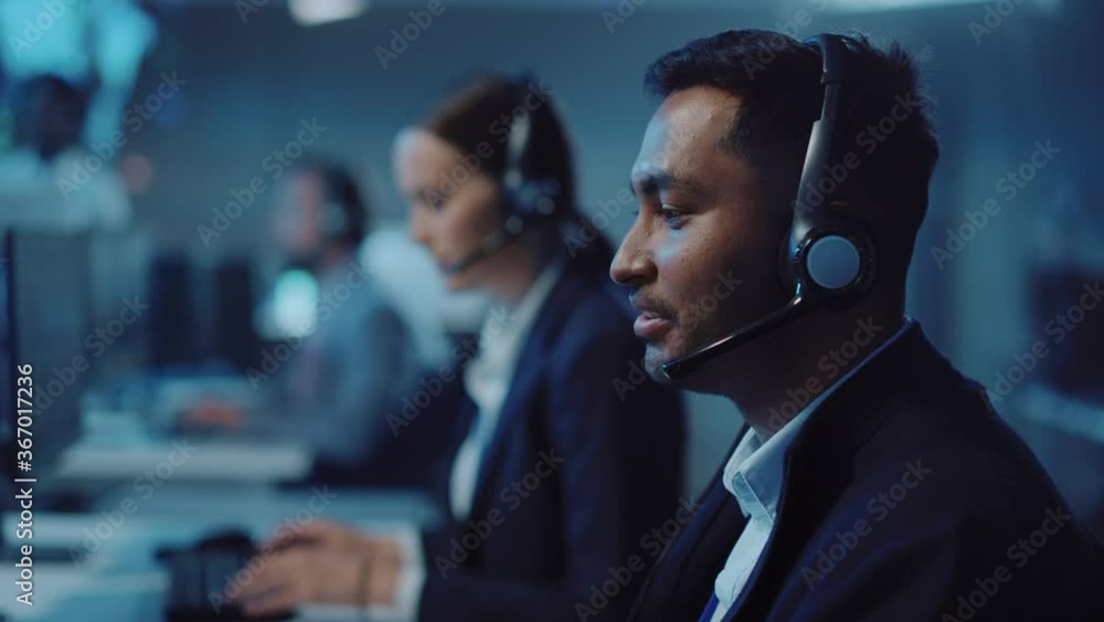 Poster Close Up Portrait of a Joyful Technical Customer Support Specialist Talking on a Headset while Working on a Computer in a Call Center Control Room Filled with Computer Display Screens and Data Servers