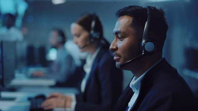 Close Up Portrait of a Joyful Technical Customer Support Specialist Talking on a Headset while Working on a Computer in a Call Center Control Room Filled with Computer Display Screens and Data Servers
