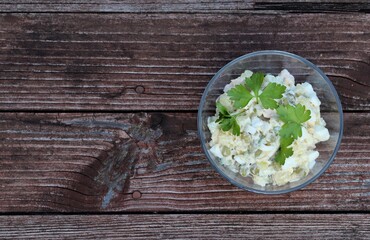 Russian salad Olivier with potatoes, chicken, eggs, cucumber, green peas in a bowl on a wooden background in rustic style top view copy space