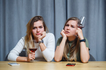 Two girls of European appearance are sitting at the table with glasses of wine. Conversation of girlfriends with alcoholic drinks.