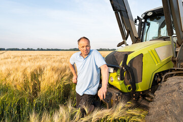Ackerbau - Landwirt steht vor einem Traktor in einem abreifenden Getreidefeld.