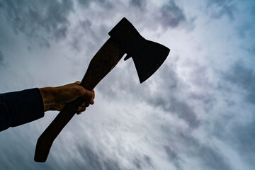 silhouette of a raised ax in hand against a gloomy sky
