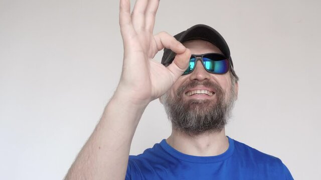Adult man in blue t-shirt and sunglasses shows OK gesture and smiles.