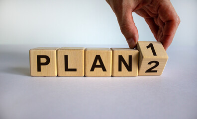 Time for Plan 2. Hand is turning a cube and changes the word 'Plan 1' to 'Plan 2'. Beautiful white background. Business concept. Copy space.
