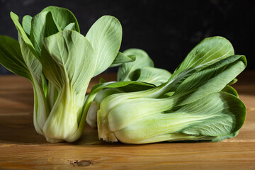 Fresh green bok choy or pac choi chinese cabbage on a gray wooden background. Dark, moody. Side view, close up, selective focus.