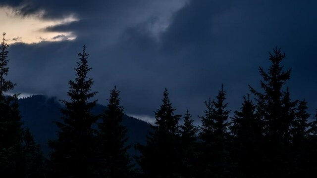Time lapse dramatic dark thunder clouds roll over mountain valley with pine forest foreground. Epic cloudscape float over the landscape before the storm