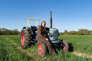 Junge Frau mit Spass an der Landwirtschaft sitzt auf einem Oldtimer - Traktor.