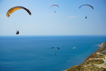 Paragliders soar on beautiful paragliders against the background of blue sky and blue sea, shot from the top of the mountains