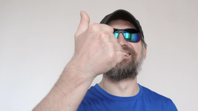 Adult man in blue t-shirt and sunglasses shows thumb up and smiles.