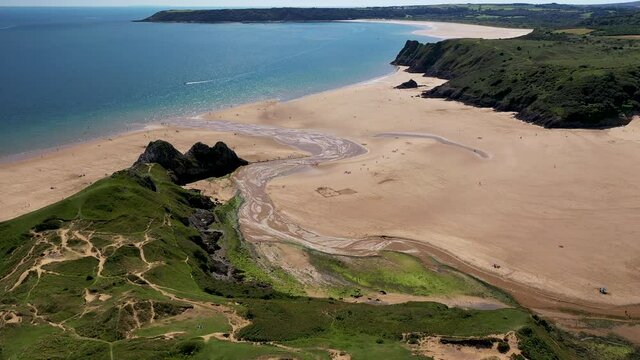 Aerial view of green foliage, large cliffs and a huge sandy beach at low tide (3 Cliffs Bay, Gower Peninsula, Wales, UK)