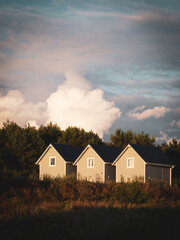 3 identical small wooden houses stand side by side in the sunset and the sky is cloudy
