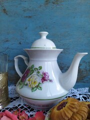 Kitchen still life white tea pot glass with cup holder cookies dry roses on the lace tablecloth on a wooden table