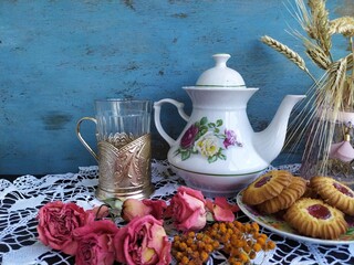 Kitchen still life white tea pot glass with cup holder cookies dry roses on the lace tablecloth on...