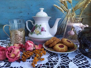 Kitchen still life white tea pot glass with cup holder cookies dry roses on the lace tablecloth on a wooden table