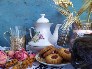 Kitchen still life white tea pot glass with cup holder cookies dry roses on the lace tablecloth on a wooden table