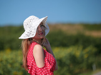 Young pretty woman in straw hat and white summer shirt posing at the sunflower's field. 