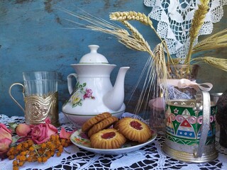 Kitchen still life white tea pot glass with cup holder cookies dry roses on the lace tablecloth on a wooden table