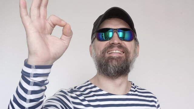 Man in sailor's stripped vest in sun glasses an smiles and shows OK gesture.