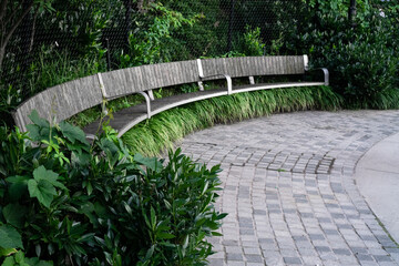 long curved wooden bench in a park against greenery background