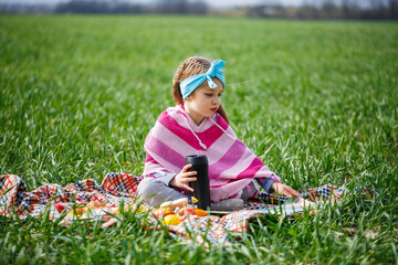 little girl child sits on a bedspread and reads a book with a fairy tale, green grass in the field, sunny spring weather, smile and joy of the child, blue sky with clouds
