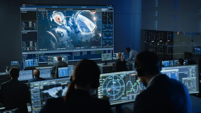 Group of People in Mission Control Center Establish Successful Video Connection on a Big Screen with an Astronaut on Board of a Space Station. Flight Control Scientists Sit in Front Computer Displays.