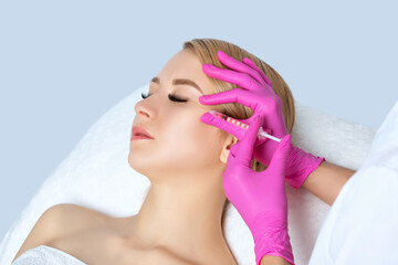 Beautiful blonde woman at the beautician.Makeup artist does anti wrinkle injections on the face, in...