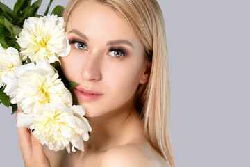 Obraz na płótnie Canvas Portrait of a beautiful blonde woman with long hair, beautiful fresh makeup and healthy clean skin with peonies in her hands. Makeup and cosmetology concept.