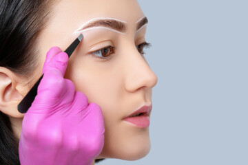 Brunette teenager girl having Permanent Make-up Tattoo on her Eyebrows. Eyelash artist plucks...