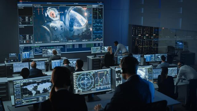 Group of People in Mission Control Center Establish Successful Video Connection on a Big Screen with an Astronaut on Board of a Space Station. Flight Control Scientists Sit in Front of Computers.