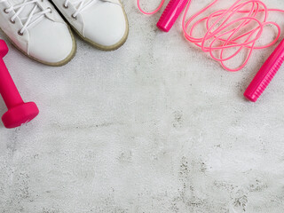 White sneakers and pink dumbbells with a rope.

White sneakers and a pink dumbbell with a skipping rope on a light concrete background with a place for text, top view close-up.