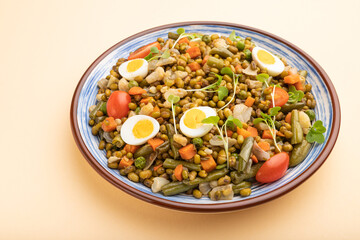 Mung bean porridge with quail eggs, tomatoes and microgreen sprouts on a pastel orange background. Side view.