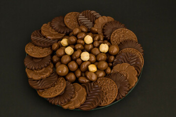 Milky and bitter round shape chocolate Madlen,designed on glass plate,at black background with hazelnuts and copy space.The Sugar Feast or any festival celebration.