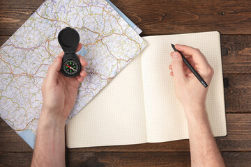 Travel planning concept. Hand writing in blank notepad with compass and map on wooden table...